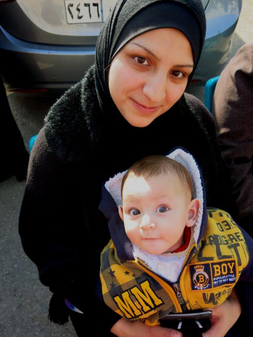Photo Meg Pruce.  Wafaa* and baby Ahmed* at the bus stop waiting to be registered for their vouchers.